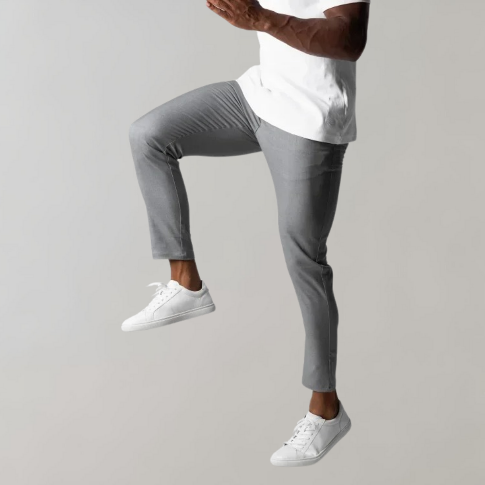 Man in gray pants and white sneakers, jumping, in front of a gray background.