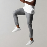 Man in gray pants and white sneakers, jumping, in front of a gray background.